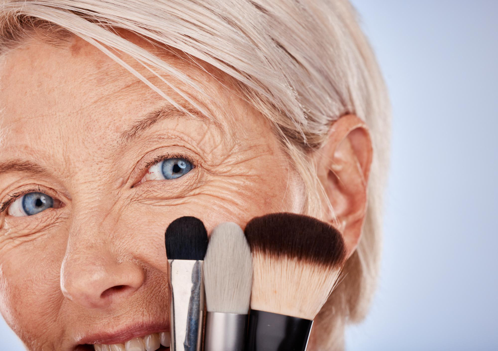 Mujer de pelo cano con brochas de maquillaje junto al rostro