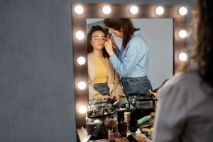 Maquilladora preparando a una presentadora ante el espejo del camerino