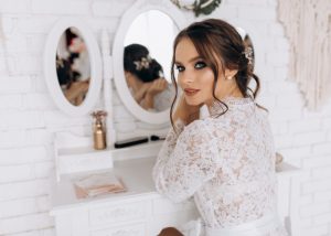 Novia maquillada con vestido de encaje frente al espejo