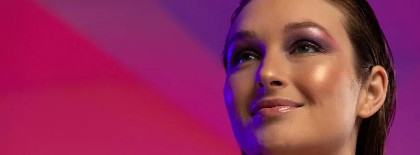 Mujer con maquillaje luminoso efecto glow bajo luces de colores