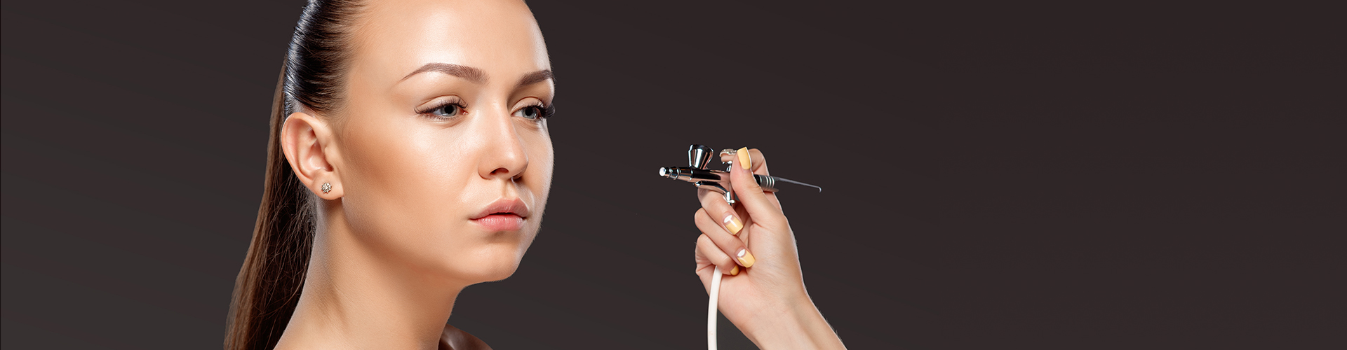 Maquilladora aplicando maquillaje con aerógrafo sobre fondo oscuro