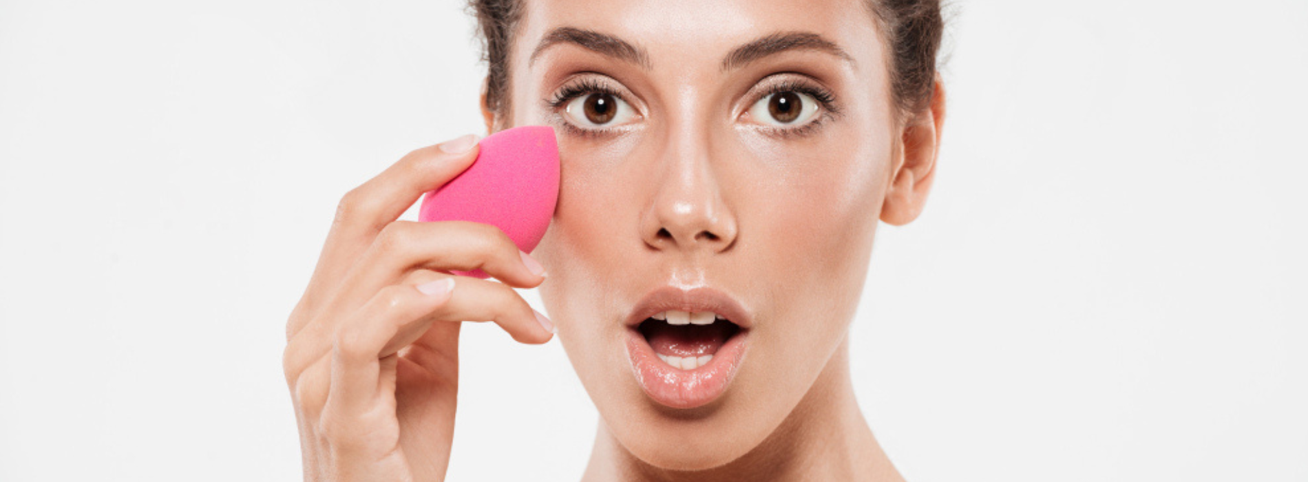 Mujer sujetando una esponja de maquillaje rosa junto a su rostro