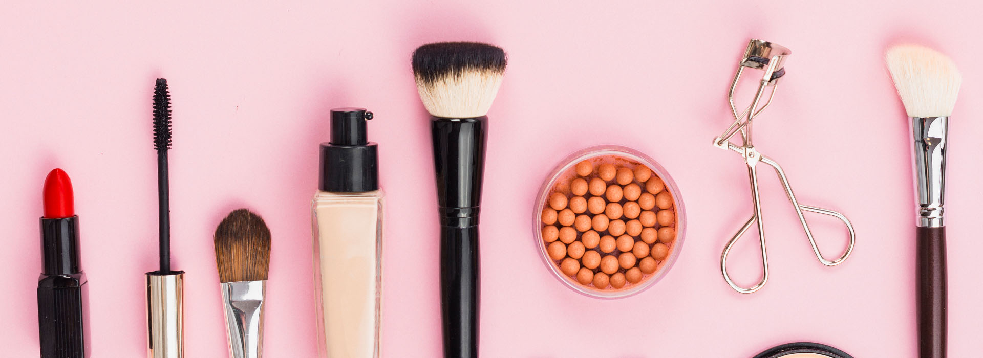 Brochas, labial y rizador de pestañas sobre fondo rosa
