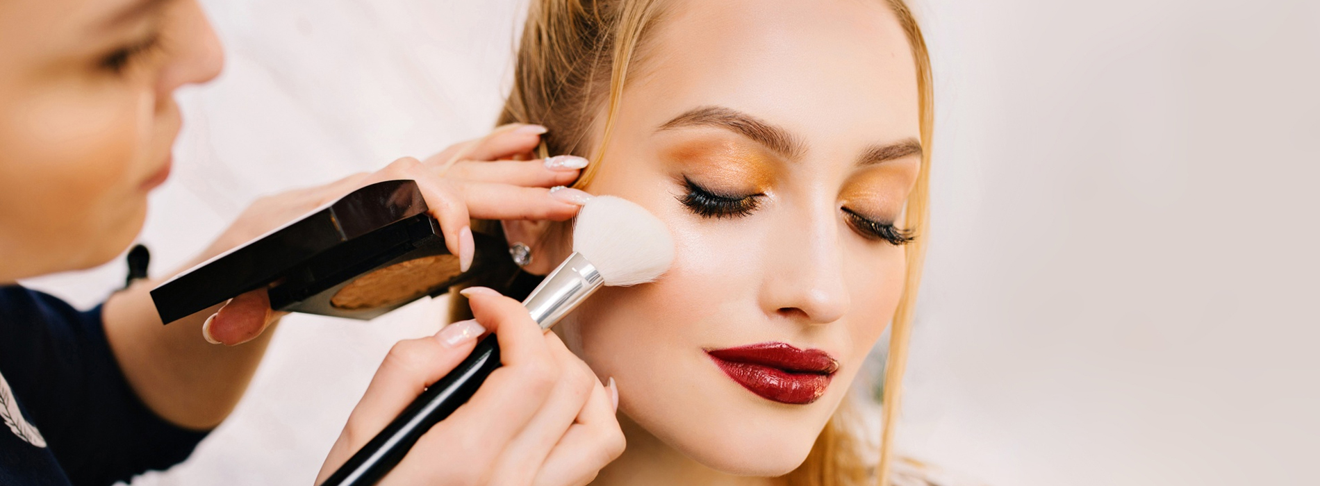 Mujer rubia recibiendo maquillaje con brocha en el rostro